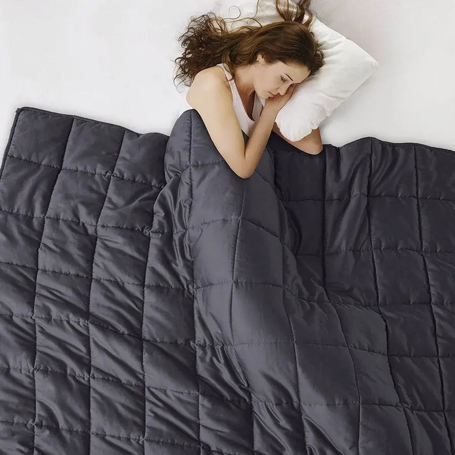 Woman sleeping under a dark gray weighted blanket on a bed.